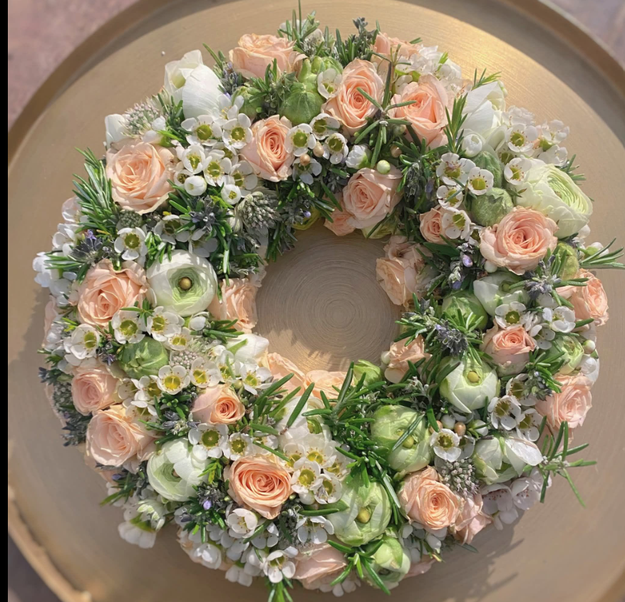 Floristischer Urnenkranz mit weißen und apricotfarbenen Blüten, zarten Lila-Akzenten und harmonischem, natürlichem Beiwerk.