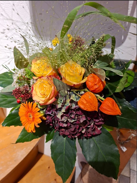 Leuchtend gelbe Rosen, orangefarbene Gerbera und Lampionblumen treffen auf dunkelviolette Hortensien und frisches Grün. Zarte Gräser verleihen dem Strauß eine natürliche Leichtigkeit – ein farbenfrohes Arrangement mit herbstlichem Charme.